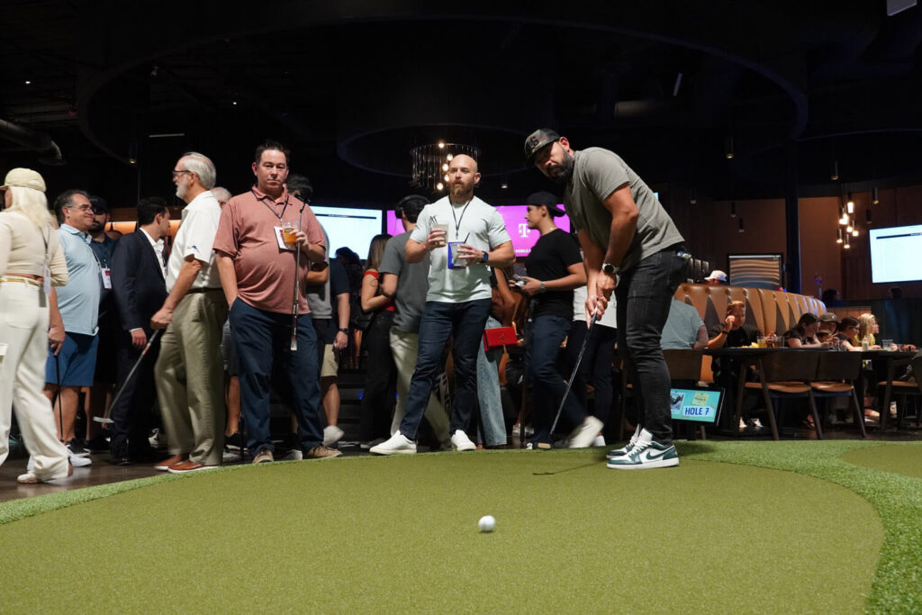 Group of guys watch anxiously as a putt rolls across the green