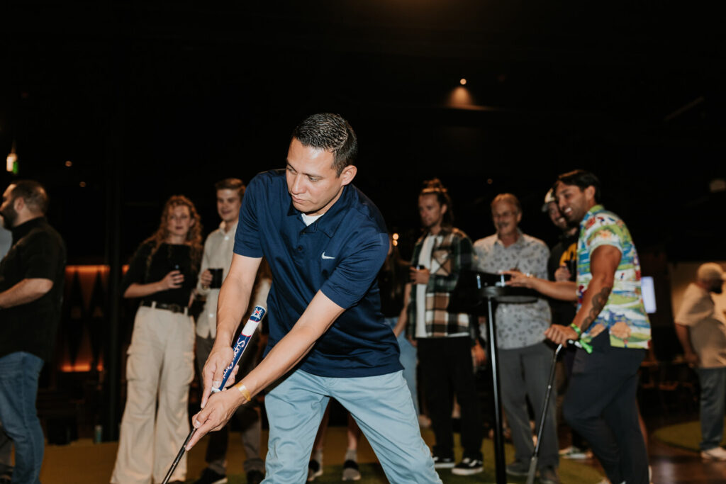 Guy strokes a putt while a crowd of people look on during a corporate private event