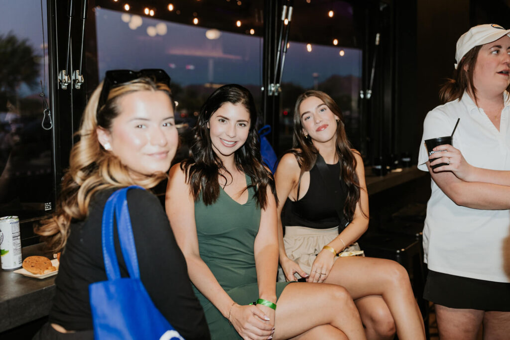 Group of three girls sitting in the Karsten Club and smiling for the camera during a group event party at Putting World